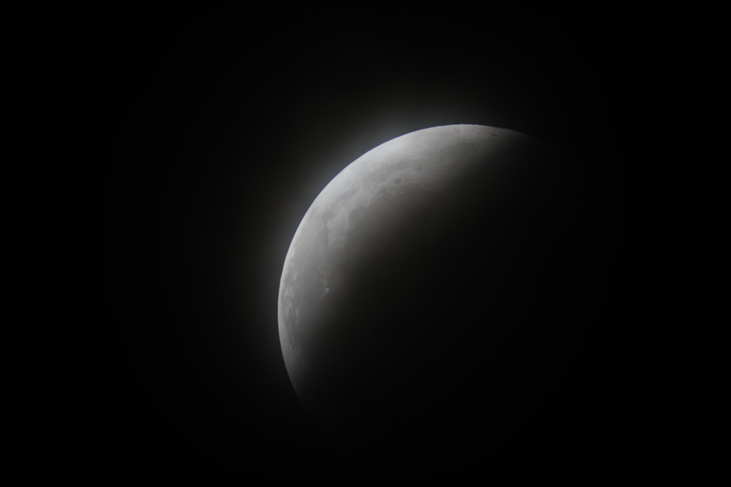 The Moon mostly covered by Earth’s shadow, with a bright crescent along its upper edge